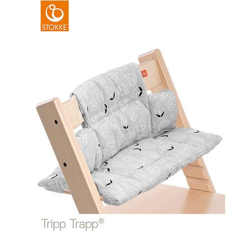 A Stokke Tripp Trapp high chair features a gray leaf-patterned cushion set, providing a stylish and comfortable seat for a baby or toddler.