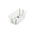 A clear plastic baby bathtub with sage green trim and a black drain plug sits at an angle, ready for bath time. 

