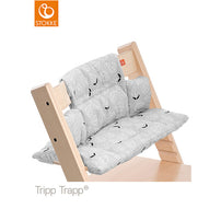 A Stokke Tripp Trapp high chair features a gray leaf-patterned cushion set, providing a stylish and comfortable seat for a baby or toddler. 
