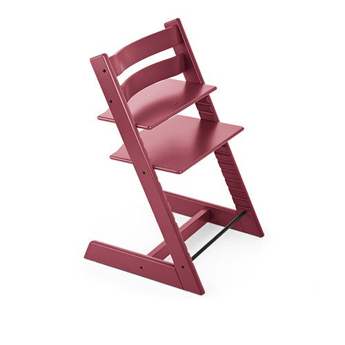 A sturdy, deep-red high chair with adjustable seat and footrest stands ready for mealtime. 

